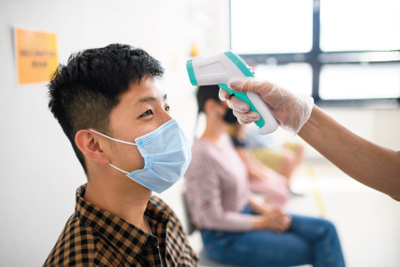 Boy wearing a face mask getting his head scanned with an infrared thermometer
