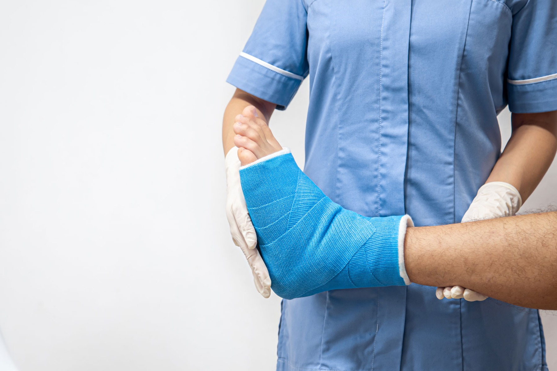 Female doctor in a blue medical gown checking broken leg on male patient.