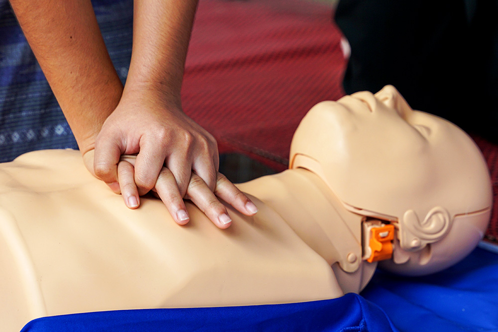 A person performing chest compressions on a CPR training mannequin, with hands interlocked and positioned in the center of the mannequin's chest