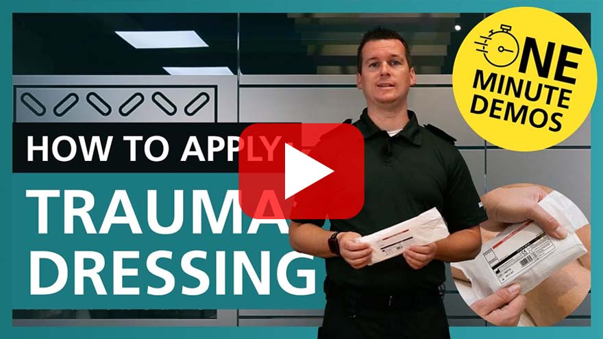 Video thumbnail featuring a person holding a trauma dressing package. Text reads 'How to Apply: Trauma Dressing' with a yellow badge saying 'One Minute Demos'. A play button is centred on the image.