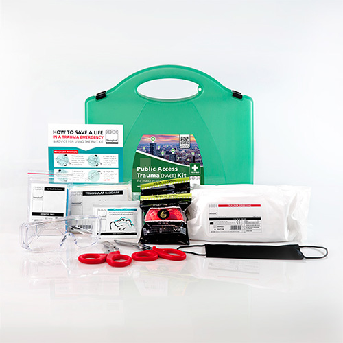 Public Access Trauma (PAcT) Kit displayed with its contents spread out. The green carrying case is positioned at the back, with various emergency supplies in front, including safety glasses, red trauma scissors, a tourniquet, bandages, a face mask, instructional leaflets, and other medical items. The kit is organised to provide essential tools for trauma emergencies.