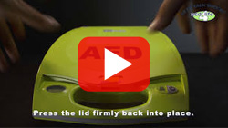 Close-up of hands setting up a ZOLL AED Plus, illustrating lid placement and setup steps.