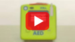 Blurred view of the ZOLL AED 3 showing the LCD touchscreen interface configuration options.