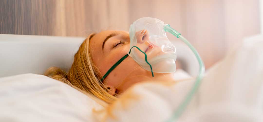 a girl lying in hospital room wearing an oxygen mask to maintain breathing