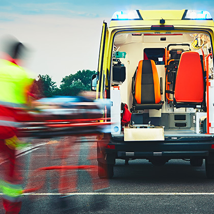 A blurred paramedic pushing a stretcher toward an ambulance with its back doors open, showing the vehicle's medical interior.