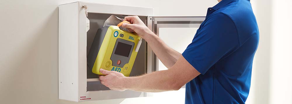 Person removing a ZOLL AED 3 from a wall-mounted cabinet, illustrating accessibility in emergencies.
