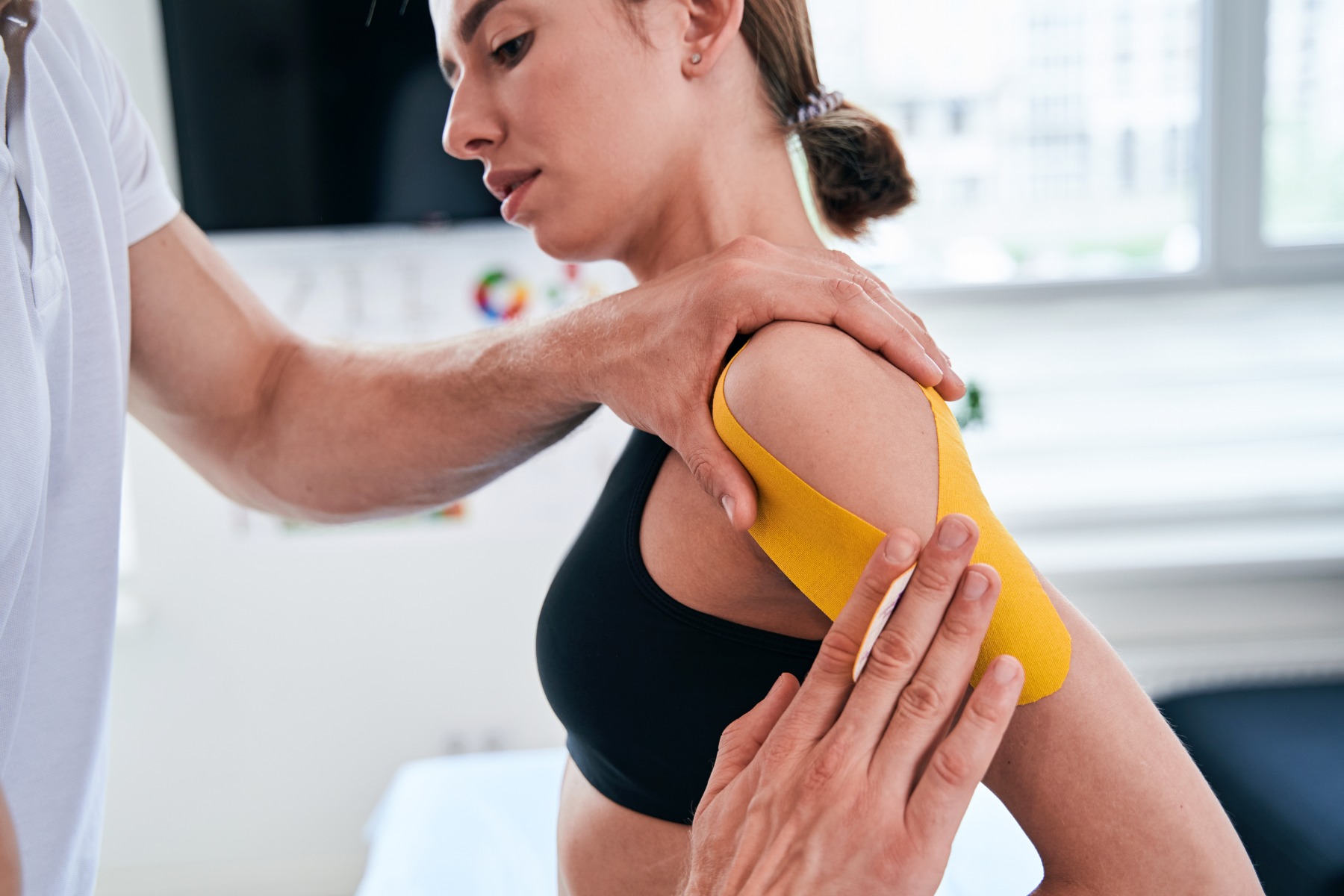 Manual therapist taping yellow tape on patient shoulder in wellness center