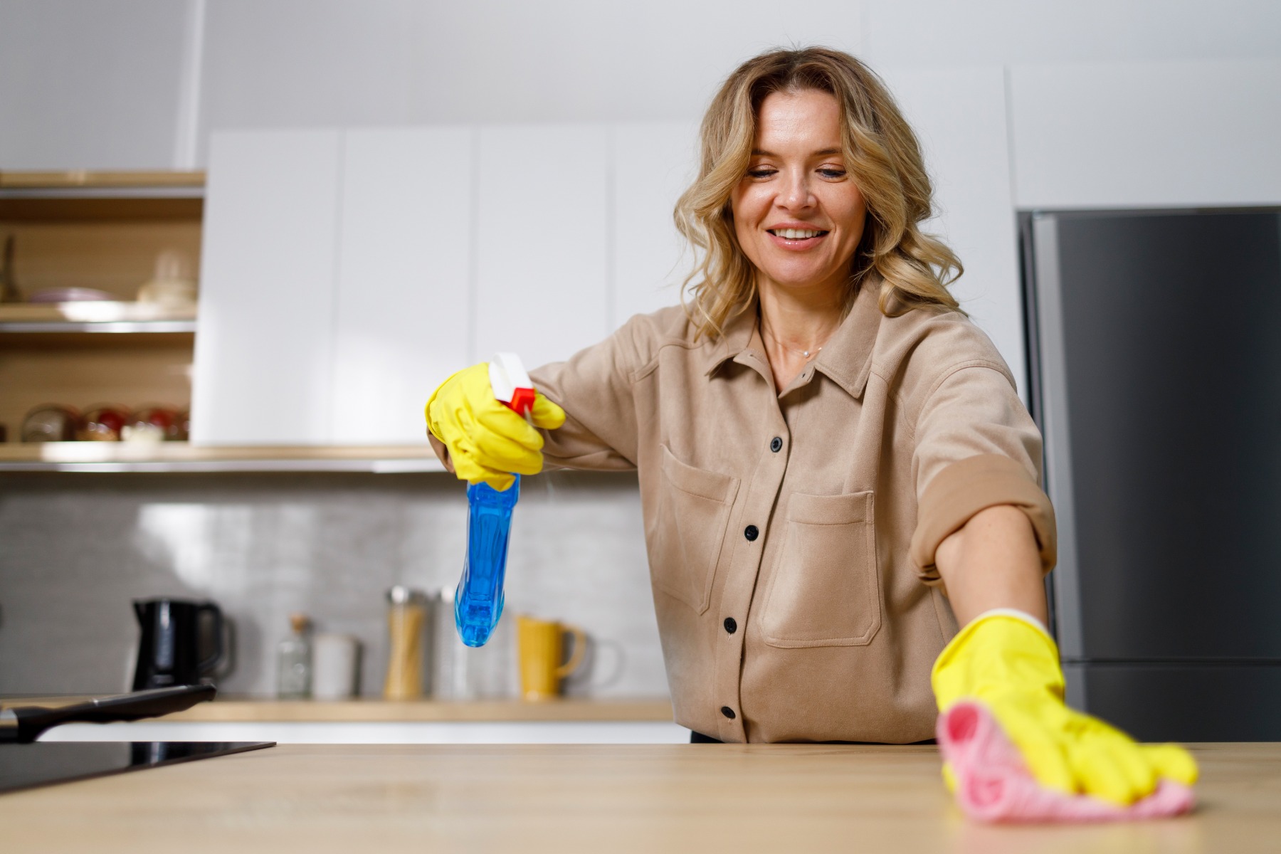 Woman spraying cleaner and disinfectant on wooden kitchen countertop while cleaning house